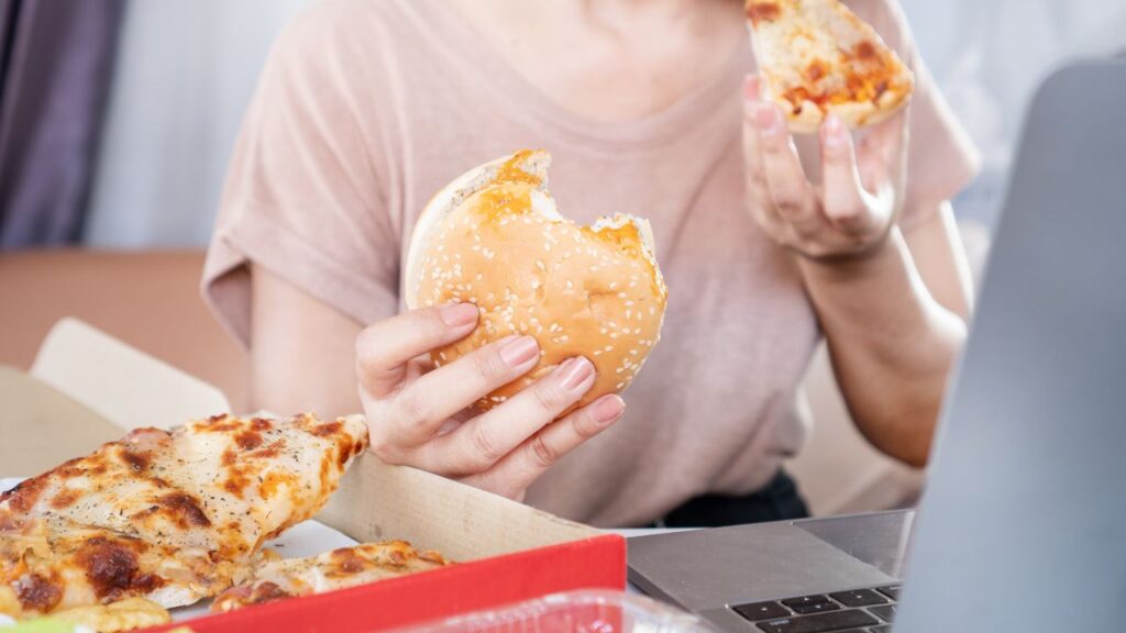 woman eating pizza and hamburguer on her desktop