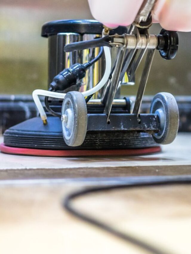 close up of a eletric broom and the feet of a person cleaning the stone floor of a elevator