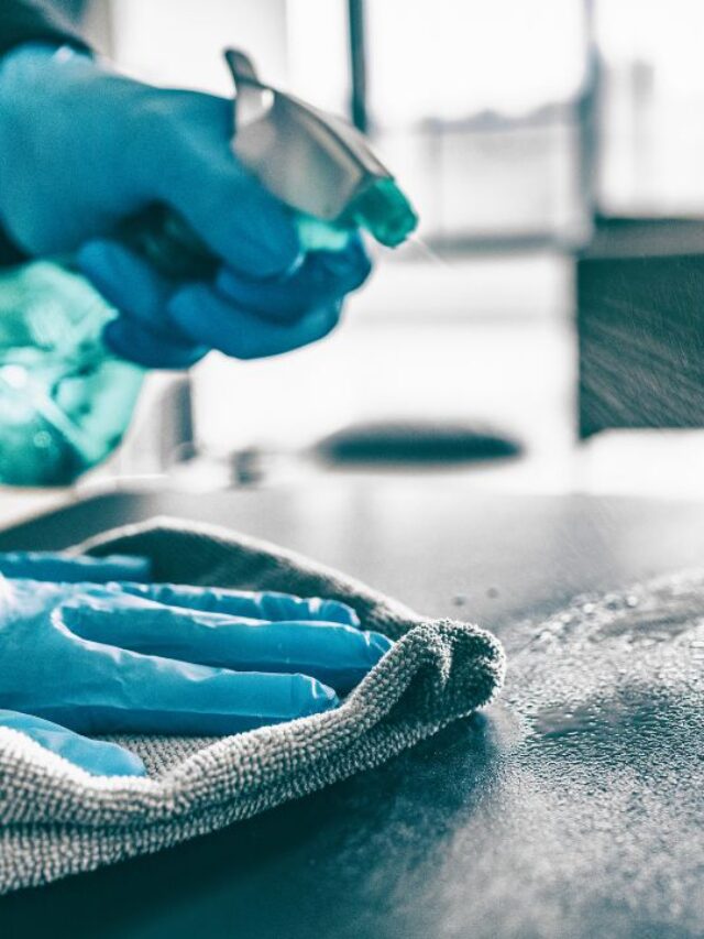 close up of hands wearing blue cleaning gloves desinfecting a desk surfice in an office environment