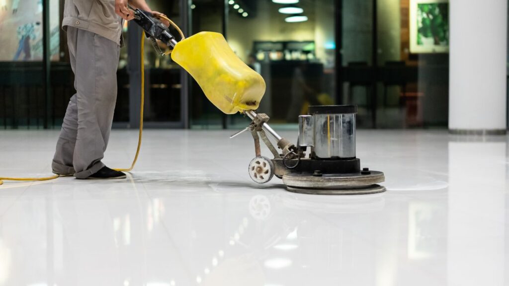 hard floor care with the image of a cropped person, showing only the legs and part of the torso cleaning a floor in a commercial building with the proper equipment