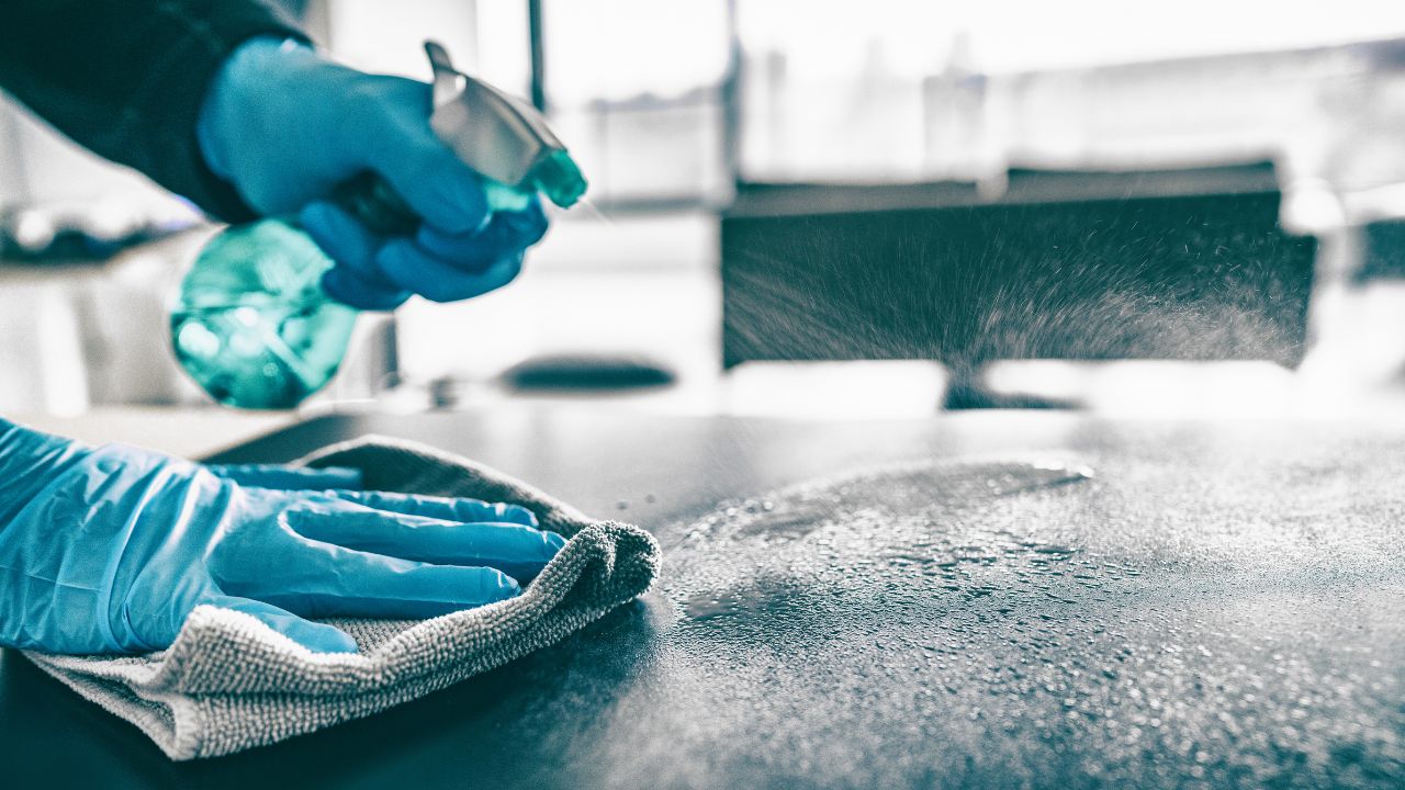 close up of hands wearing blue cleaning gloves desinfecting a desk surfice in an office environment