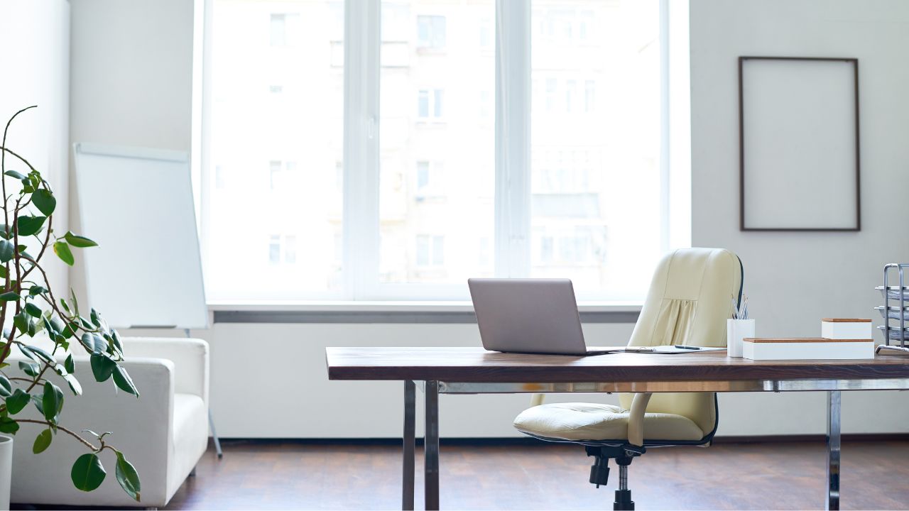 a clean and de-clutter office space with a white chair, desk, walls and curtains and a small plant to the side