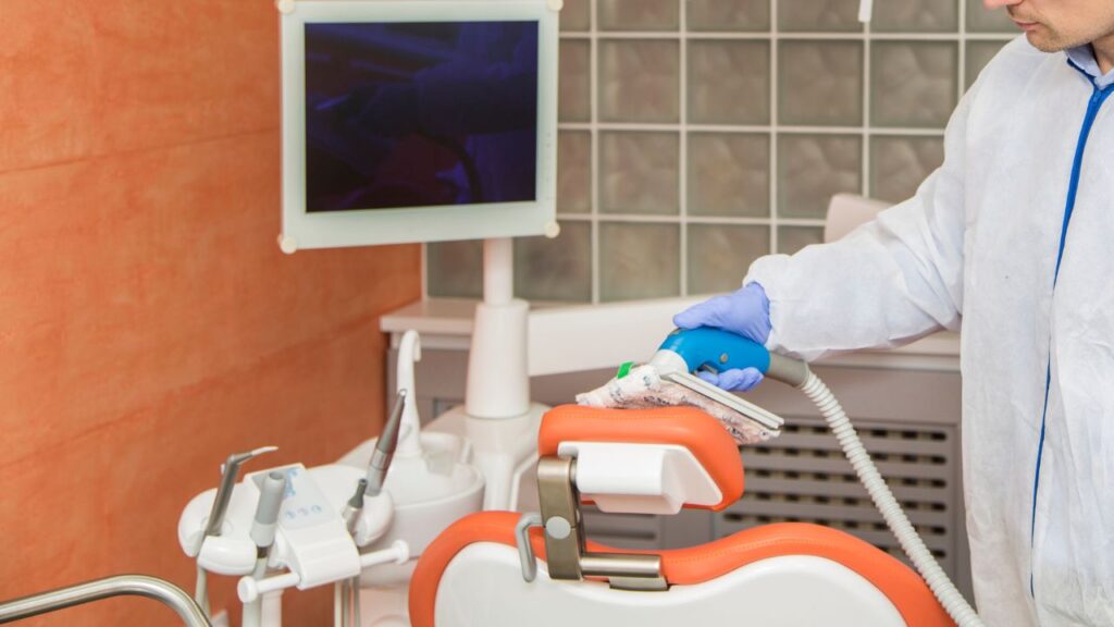 man cleaning a dental office chair with a portable vaccum cleaner