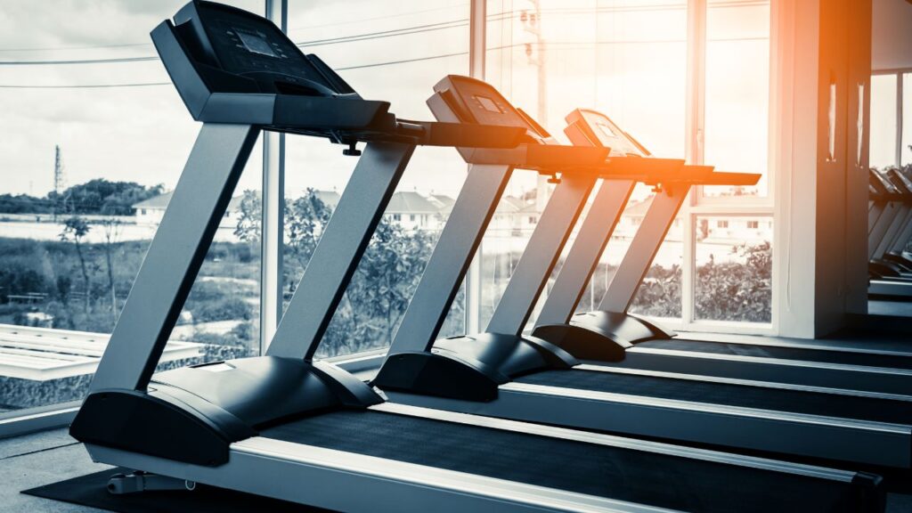 cardio machines aligned side to side in front of floor to ceiling windows at the gym