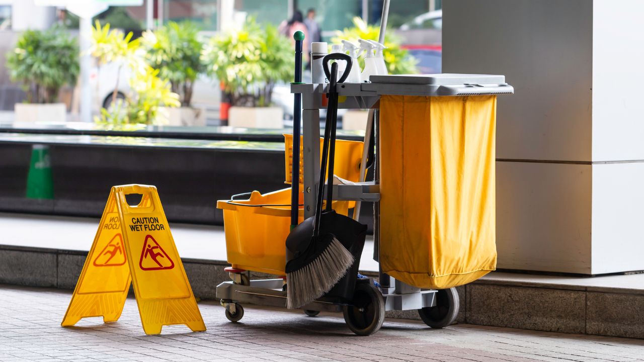 janitorial cleaning services cart with a mop, cation sign, broom and cleaning products to prevent falls