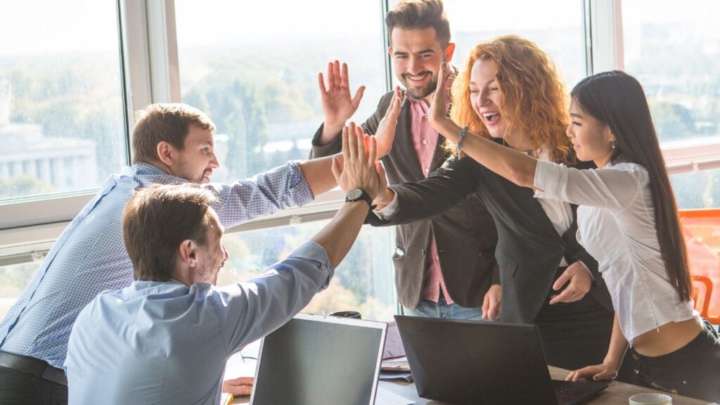 five people, three man and two women, high-fiving at an office meeting room