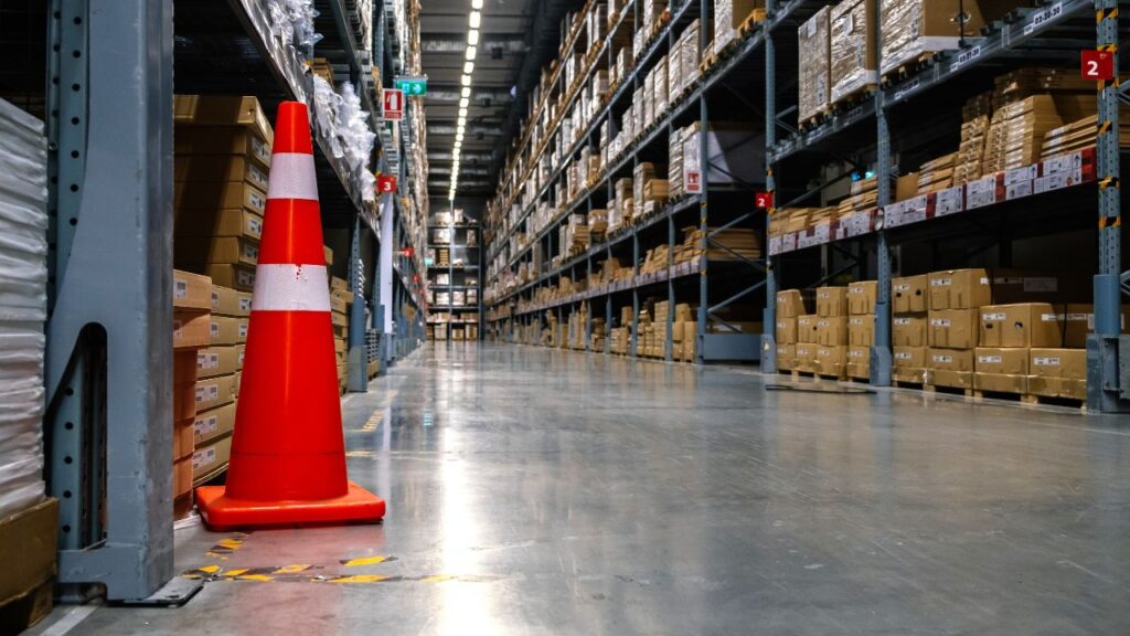 picture of an aisle inside a store showing a traffic cone and some cardboard boxes on shelves