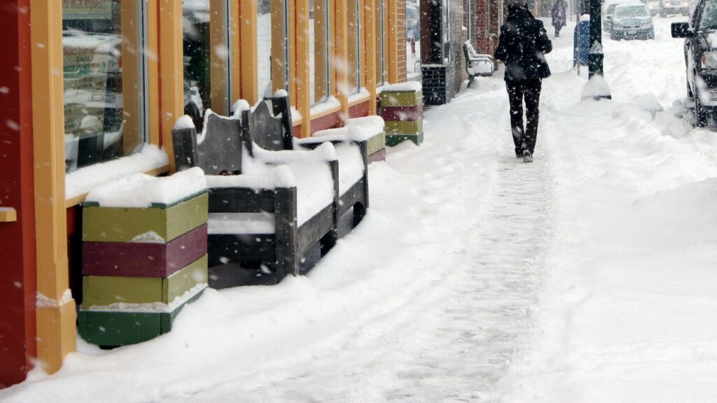 person walking in a snowy sidewalk in front of a few stores