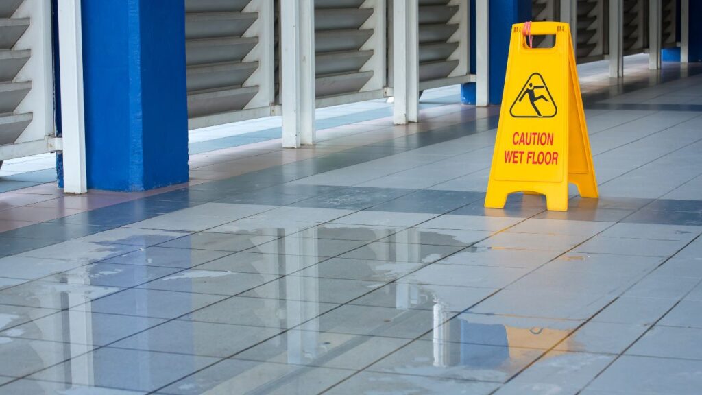 janitorial staff can prevent slip and falls by using wet floor caution signs like the one displayed in the picture with a patch of water from shower stalls