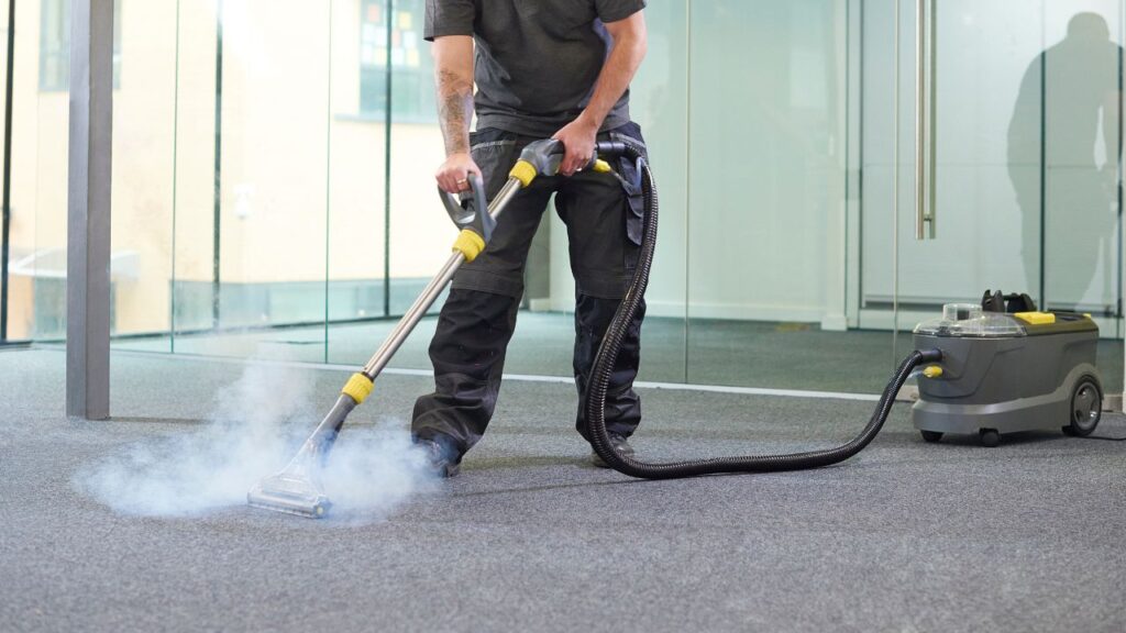 professional cleaning staff member washing a carpeted floor in a office with the method called steam cleaning used a lot in carpet cleaning commercial services