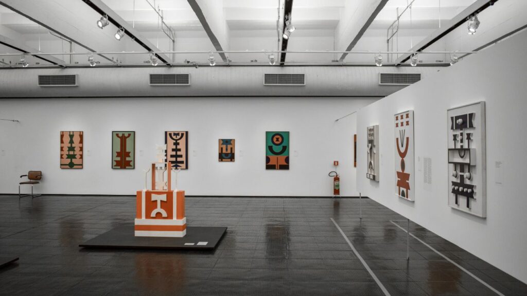 clean art exibition space with tribal paintings and a sculpure