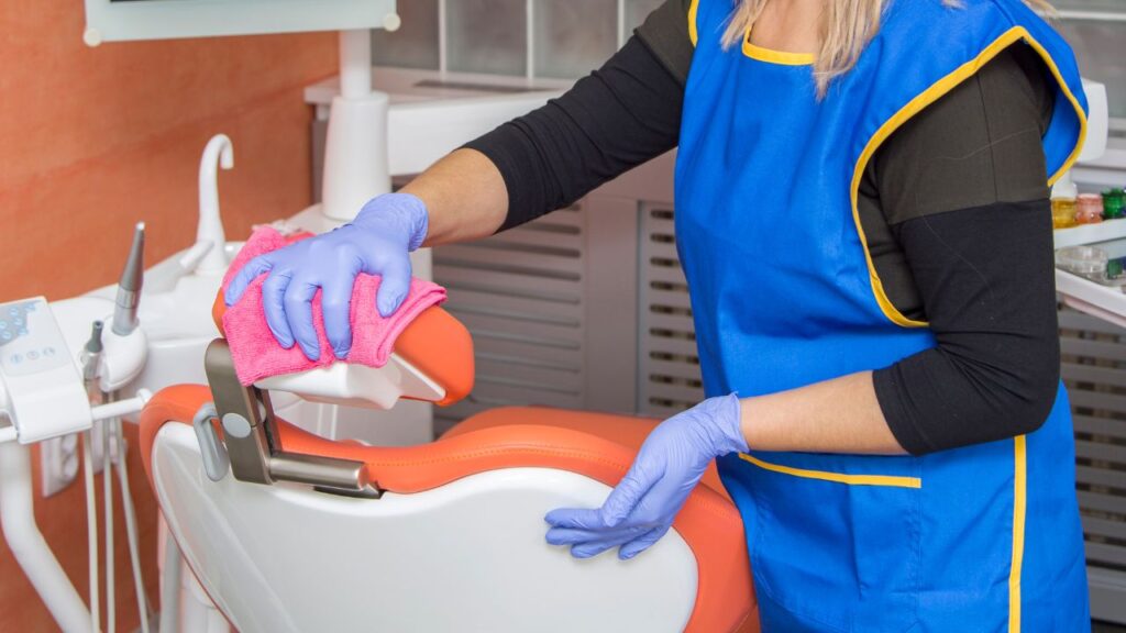 woman cleaning a dental office chair with a pink cleaning cloth