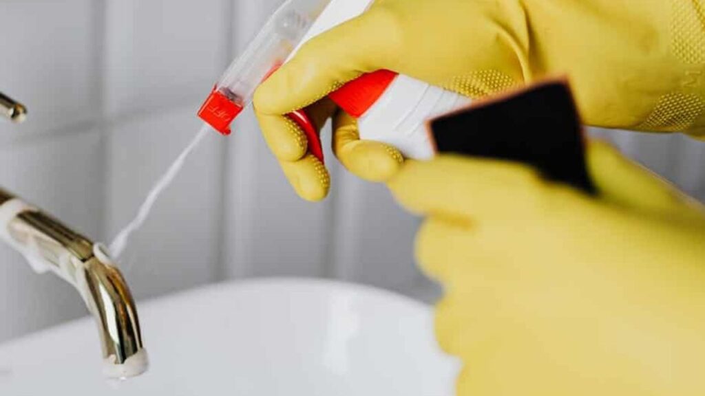 close-up of two hands wearing cleaning gloves, using a desinfecting spray to clean a restroom sink