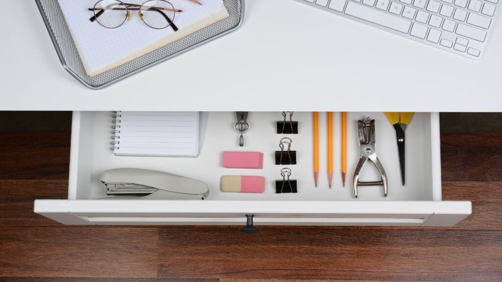 office desk with an oper drawer with some suplies inside, like a strappler, notebook, erasers and pencils