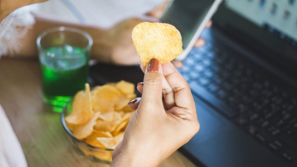 a laptop with a bowl of chips beside it and a person eating some out of the bowl