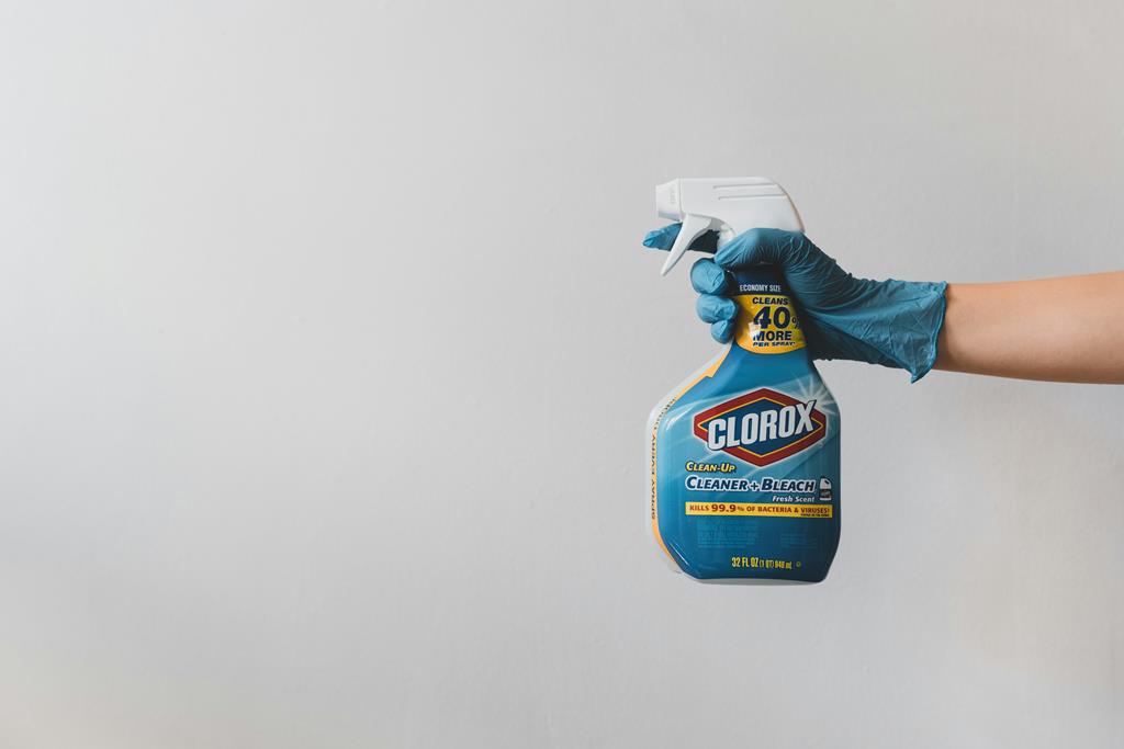 image of a sanitizer being held by a hand with a blue cleaning glove against a gey wall