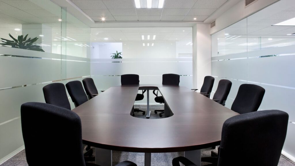 metting room with surrounding glass windows and a dark wooden desk with black cushioned chairs around it